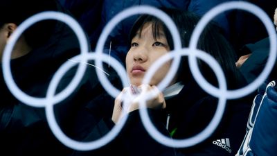 De olympiske ringene reflektert i et glass. En kvinnelig tilskuer sitter bak glasset og ser på mixed double-semifinalen i curling mellom Canada og Norge under de olympiske vinterlekene i Pyeongchang, Sør-Korea.