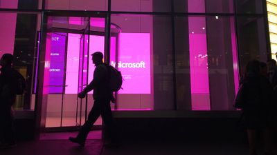 Silhuett av mennesker som går foran opplyste vinduer med stor Microsoft-logo, ved Microsofts kontor i New York.