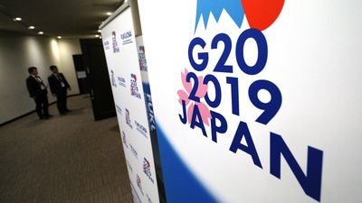 Korridor, mennesker snakker sammen, stor plakat med "G20 2019 Japan" i forgrunnen.