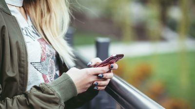 Kvinne holder mobiltelefon i hånden. Utendørs. 
