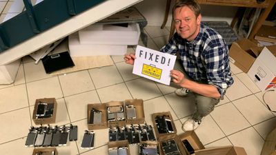 Henrik Huseby sitter på huk med flere mobiltelefoner på gulvet rundt seg, og et skilt i hendene hvor det står "Fixed!"
