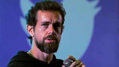 Jack Dorsey med en mikrofon i hånda, med en Twitter-logo som dekker hele bakgrunnen. 