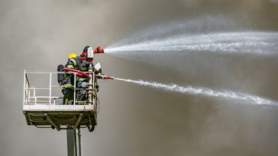 Firefighters extinguish a fire by the top of the building.