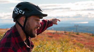 Mann med hjelm på fjell i høstfarger peker mot utsikt 