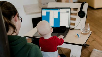 Ung mor med baby på fanget har hjemmekontor på stuegulvet. 