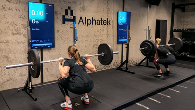 To kvinner trener med vektstenger foran dataskjermer.
