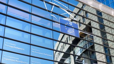 En av EU-bygningene i Brussel, speiler seg i en glassfasade med et EU-flagg på.