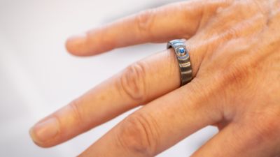 En kvinnehånd med en ring på ringefingeren, grå med en blå stein og bølger i metallet.
