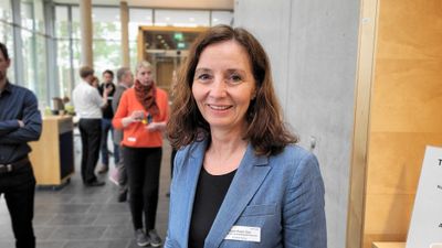 En kvinne i blå dressjakke står i et resepsjonsområder og smiler til kamera