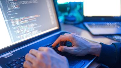To hender på en laptop som viser kode på skjermen.