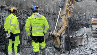 To menn i gule arbeidsklær i Implenias byggegrop på Fornebu