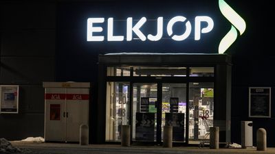 Inngangen til en Elkjøp-butikk. Det er mørkt og Elkjøp-logoen over inngangen lyser opp bildet.