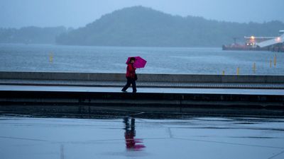 Person med paraply går langs vannkanten i Oslo sentrum.