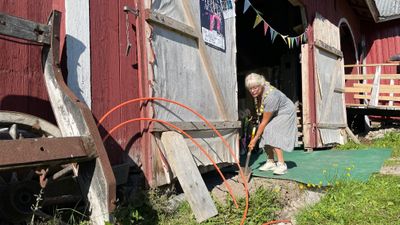 En kvinne står med spade foran en låve.