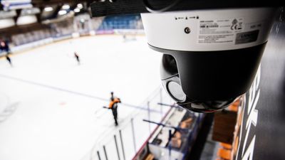 Et overvåkingskamera montert under taket, i bakgrunnen ser vi en ishockeybane med et par spillere.