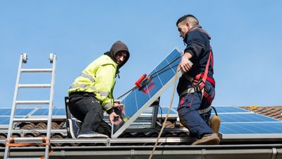 To menn monterer solceller på tak.
