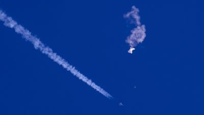 En hvit ballong er ødelagt og faller fra blå himmel, et jagerfly kommer forbi.
