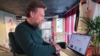 En mann sitter på en kafe med en laptop i fanget, vi ser en nettside med Grønne tips slått opp på laptoppen.