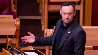 En mann i mørk dress og skjorte på talerstolen i Stortinget. på jakka en SV-button.