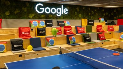 Et bordtennisbord foran Google-logo og mange puter med logoer fra Google-produkter.