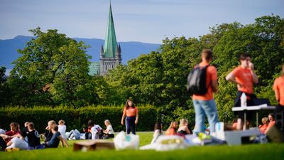 Studenter koser seg på en plen, i bakgrunnen nidarosdomen.