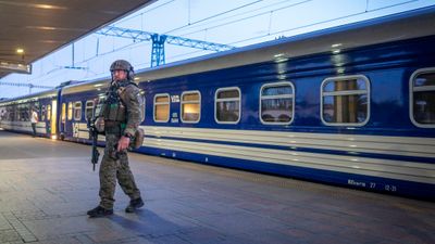 En mann i uniform og med våpen står på en perrong foran et blått tog.