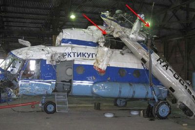 Skadene på helikopterets venstre side. Halerotoren og den uskadede støtten bakerst på halebommen er merket med røde piler. 
