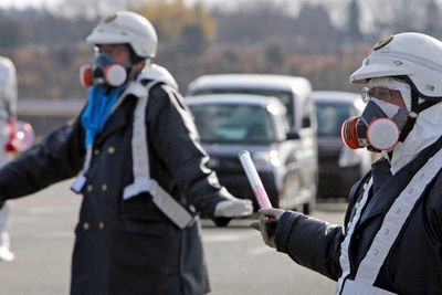 Politimenn med gassmasker leder trafikken vekk fra kjernekraftverket Fukushima Daiichi 1 under evakuering i mange kilometers radius etter radioaktive utslipp grunnet lørdagens eksplosjon ved anlegget. Nå trues tre av reaktorene av nedsmelting.
