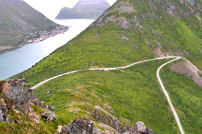 Bildet viser fylkesveg 86 over toppen av Ballesvikskaret. Fiskeværet Gryllefjord kan ses i bakgrunnen til høyre.