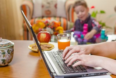 Detail of a woman hands writing in notebook and boy playing on the background. Home office concept.