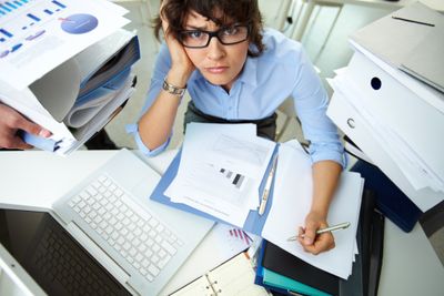 Perplexed accountant doing financial reports being surrounded by huge piles of documents