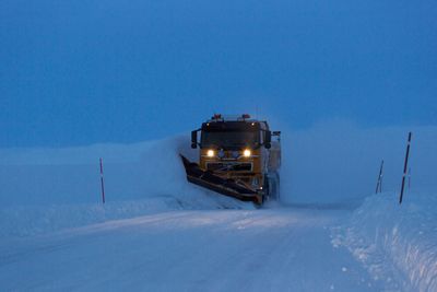 Snøbrøyting i blåtimen. Brøytebil på riksvei 890 Kongsfjordfjellet. Tana kommune. Finnmark.Snow Plough in the blue hour on a mountain road at Finnmark County. Northern Norway.