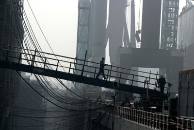 En kinesisk verftsarbeider går over broen som leder til et fraktskip for råolje på Dalian New Shipbuilding Heavy Industry Co. Ltd i Dalian i nordøstlige Kina.