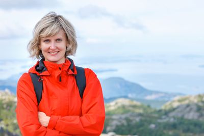 Portrait of happy woman tourist standing smiling outdoors against stunning landscape of Norway