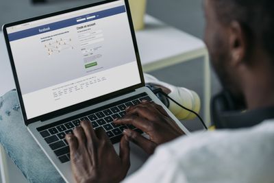 cropped shot of young african american man using laptop with facebook website on screen