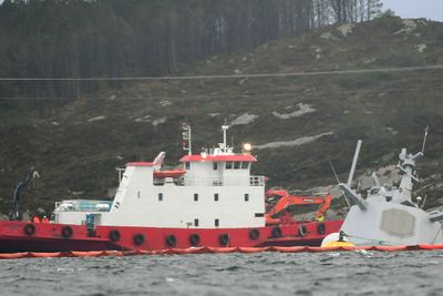En båt med bergingsmannskaper ved den havarerte fregatten. Helge Ingstad ligger nå nesten helt under vann, etter at flere vaiere som har holdt skipet fast, har løsnet.