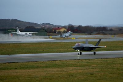 En F-35A takser på Ørland flystasjon samtidig som et F-16 tar av. På den sivile sida står et ATR-42 parkert.
