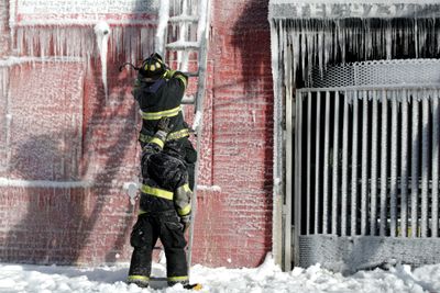 En brannmann støttes opp av en kollega mens kan kapper is av en stige etter å ha bidratt til å slukke en boligbrann i Newark, USA.