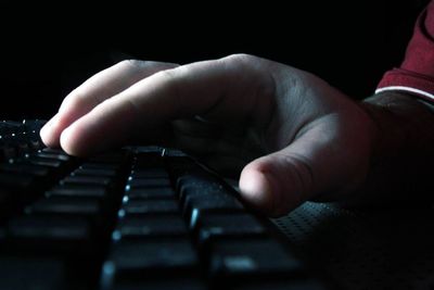 Nærbilde av hånd i mørket, over et tastatur. hacking, pirat, nettkriminalitet