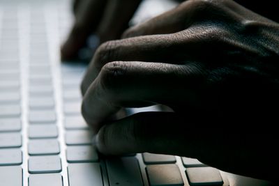 closeup of a young man typing in a computer keyboard in gloom, with a dramatic effect