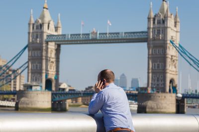 Businessman talking on mobile phone outdoor, looking at Tower Bridge in London city, UK.