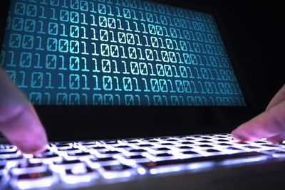 Hacker writing virus code with laptop in dark. Data crimimal in shadow. Cyber security, internet fraud and phishing concept. Close up of hands on keyboard and computer screen with binary numbers.