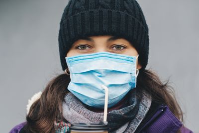 Woman with face mask drinks coffee outdoors. Coronavirus epidemic in city. Face mask protective for spreading of coronavirus. COVID-19 pandemic coronavirus. Woman in city street wearing face mask.