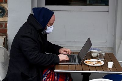 Fjernarbeid under koronapandemien bidrar til et PC-salg verden ikke har sett på ti år. Bildet viser en mann med ansiktsmaske som jobber fra en kafé i London, rett før julen 2021.