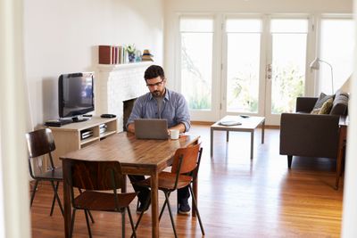 Man Working From Home Using Laptop On Dining Table