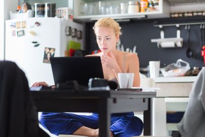 Female freelancer in her casual home clothing working remotly from her dining table in the morning.  ...