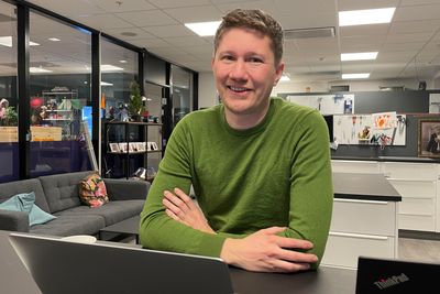 Mann smiler i kontorlandskap grønn genser brunt hår