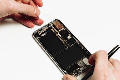 Smart Phone Battery Change Repair Maintenance. Repairman Hand Fix Smartphone Back Part Disassemble with Tweezers. Mobile Cellphone Assembly. Technician Work at White Workplace Copy Space View