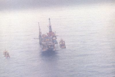 Bilde av boligplattformen Alexander Kielland dagen etter at den mistet ett av beina og kantret i Nordsjøen den 27. mars 1980. På bildet ser man de fire gjenværende beina på den veltede plattformen som stikker opp av vannet.
