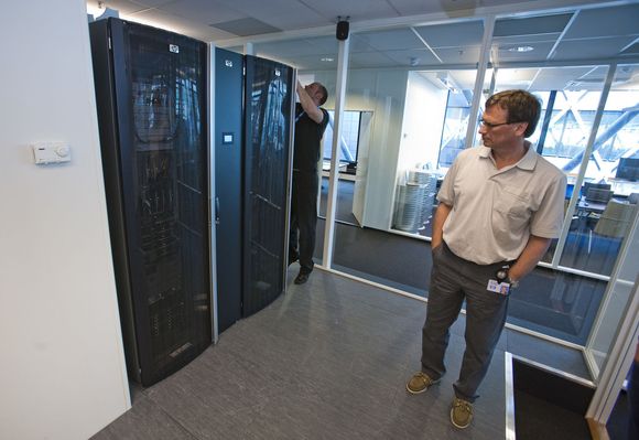 Datarommet bak møterommet i HPs «Enterprise Technology Center» innholder to rack med bladservere og lagring. Mellom rackene er et smalere skap: kjølemodulen. Det lysende feltet midt på kjølemodulen viser driftstemperaturen. Gaute Ledang mekker, Jan Fredrik Gunvaldsen står foran. <i>Bilde: Per Ervland</i>